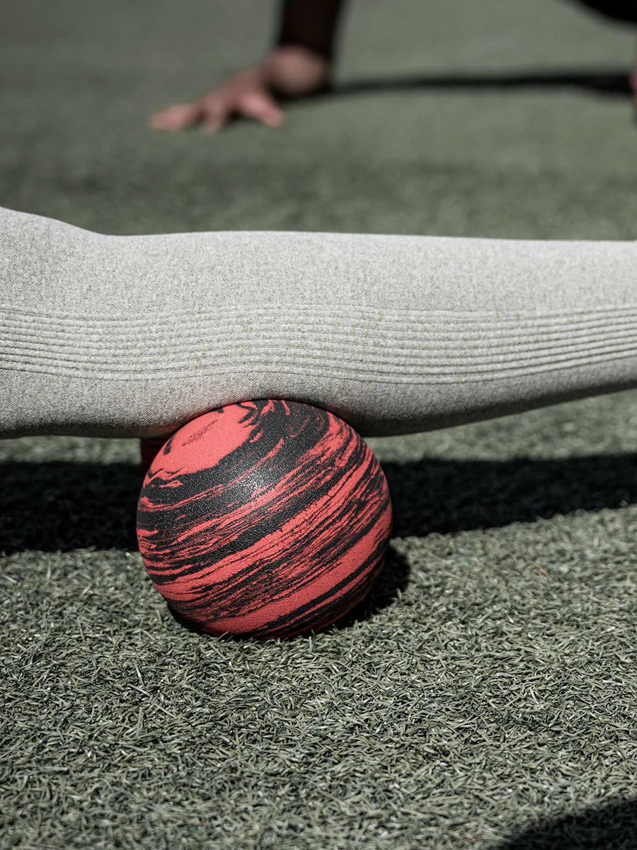 Person holding a red and black striped ball on a grassy surface. Roller-Peanut-Foam-COREFX Red and black marbled object on a white background